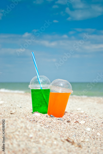 Two cocktails drink sand close-up against the background of the sea and sky, clouds a glass a tube for drinking liquid, soda summer sun weekend rest vacation, shore a wave of foam shells still lif