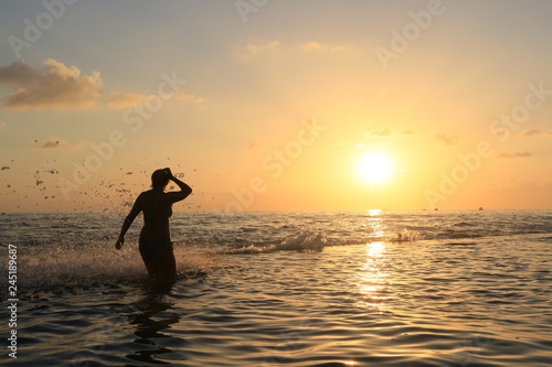 Fototapeta Naklejka Na Ścianę i Meble -  The figure of a woman on the sea with a high wave and spray on the background of a golden sunset.