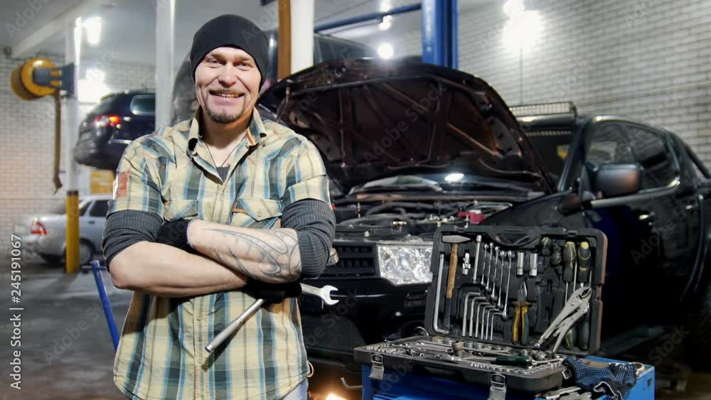 Car service. Brutal mechanic man standing by the car and grins Car service. Brutal mechanic man standing by the car and grins