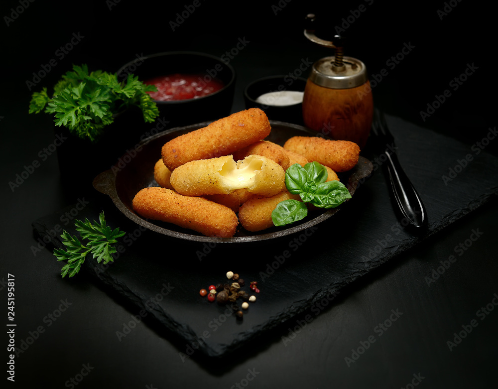 Delicious breaded mozzarella cheese sticks in a pan against a dark background Delicious breaded mozzarella cheese sticks in a pan against a dark background
