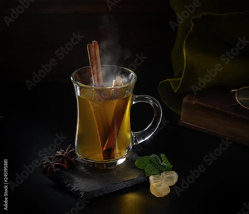 Green tea with cinnamon sticks in a glass cup on a dark background. Anise and sugar on black slate
