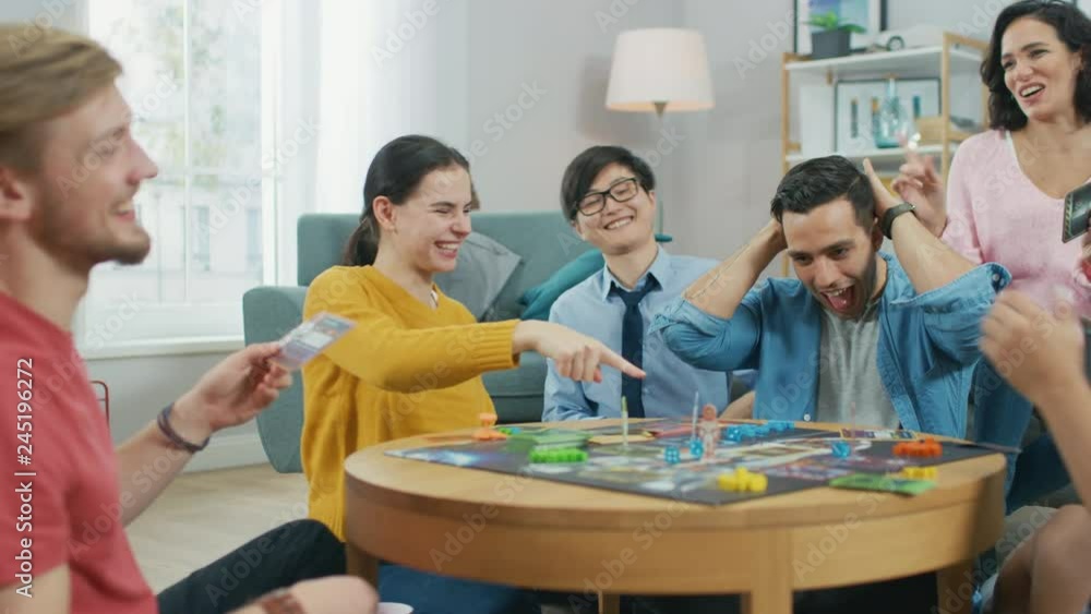 Diverse Group of Guys and Girls Playing in a Strategic Board Game with Cards and Dice. Reading Cards and Laughing. Friends Having Fun. Cozy Living Room in a Daytime Diverse Group of Guys and Girls Playing in a Strategic Board Game with Cards and Dice. Reading Cards and Laughing. Friends Having Fun. Cozy Living Room in a Daytime