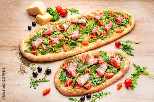 Flatbread pizza garnished with fresh arugula on wooden pizza board