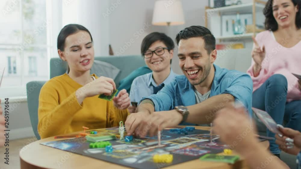 Diverse Group of Guys and Girls Playing in a Strategic Board Game with Cards and Dice. Team Players Do High Five. Cozy Living Room in a Daytime Diverse Group of Guys and Girls Playing in a Strategic Board Game with Cards and Dice. Team Players Do High Five. Cozy Living Room in a Daytime