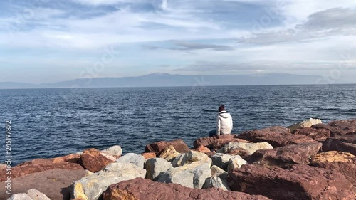 Young attractive man sitting on red rocks by the sea.