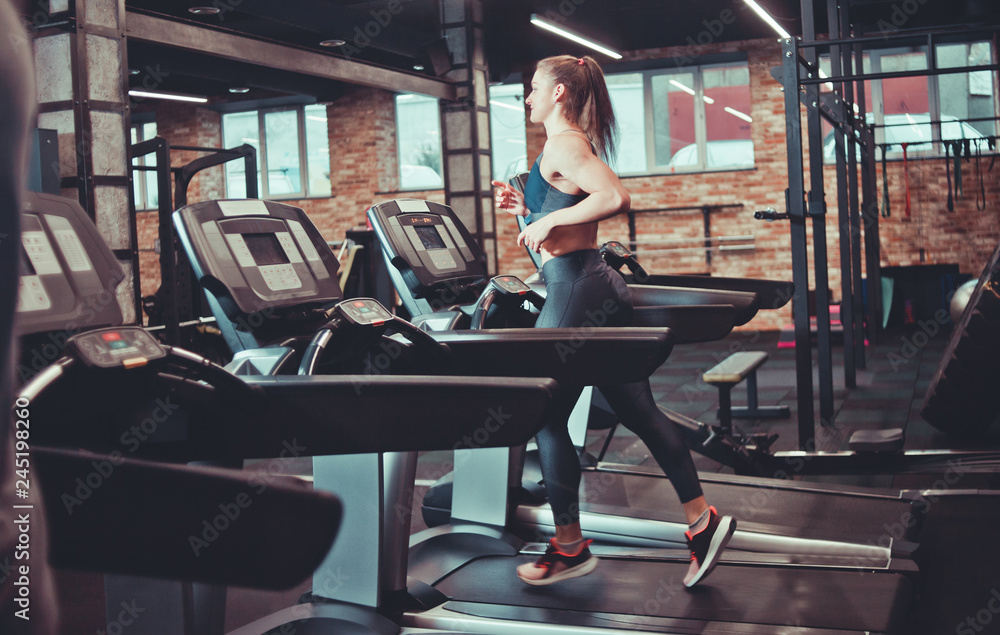 Fototapeta premium Young sports woman doing cardio training on treadmill. Running on treadmill at gym.