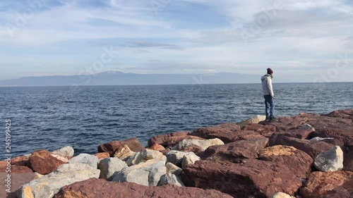 The blue color of the sea and red rocks what a beautiful view said the standing attractive young man to the sea  