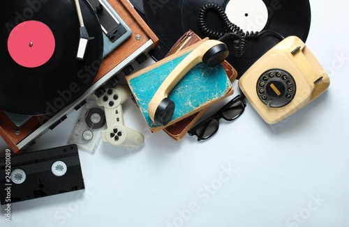 Retro 80s pop culture objects on white background. Copy space. Rotary phone, vinyl player, old books, audio, video tapes, 3d glasses, gamepad. Top view. photo