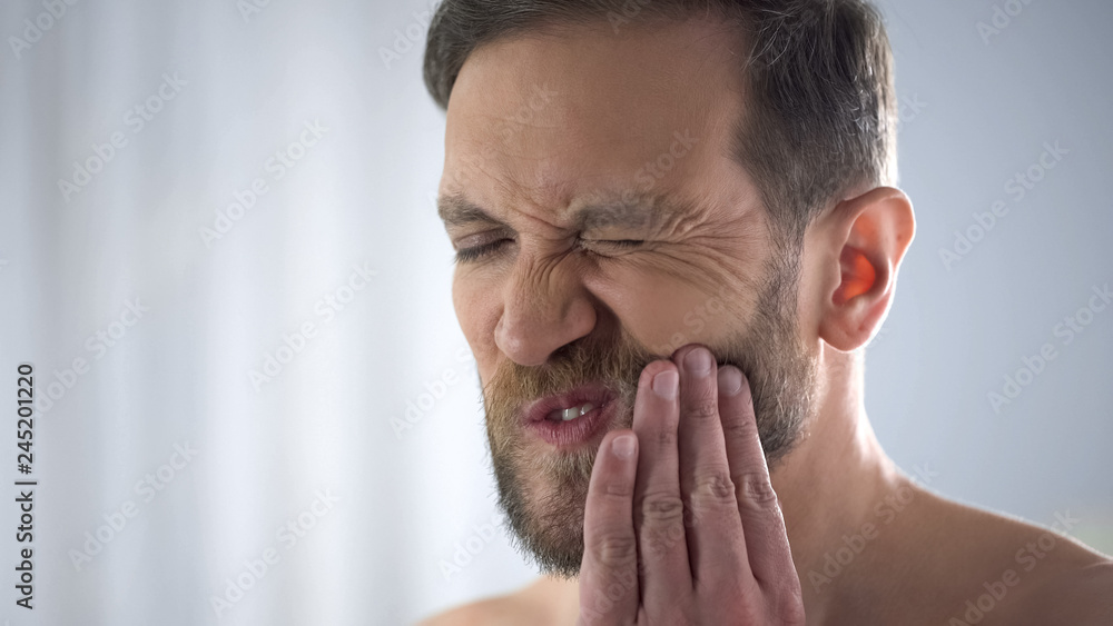 Young man touching his cheek, suffering from terrible toothache, sensitivity Young man touching his cheek, suffering from terrible toothache, sensitivity