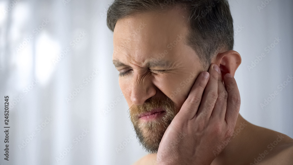 Man holding his aching ear, suffering from otitis, sudden hearing loss, close up Man holding his aching ear, suffering from otitis, sudden hearing loss, close up
