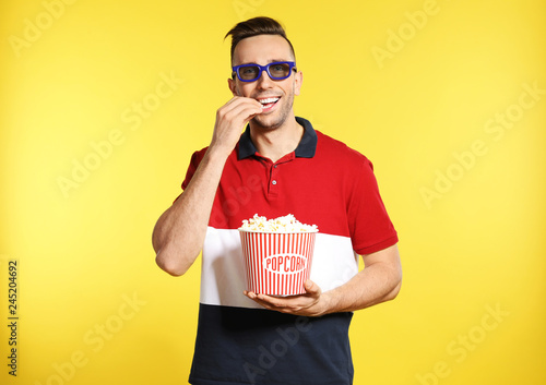 Man with 3D glasses and popcorn during cinema show on color background