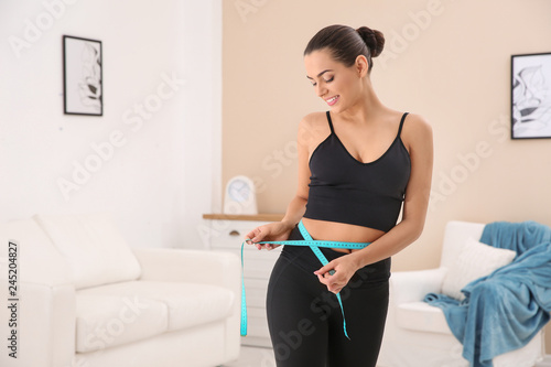 Slim woman measuring her waist at home, space for text. Weight loss