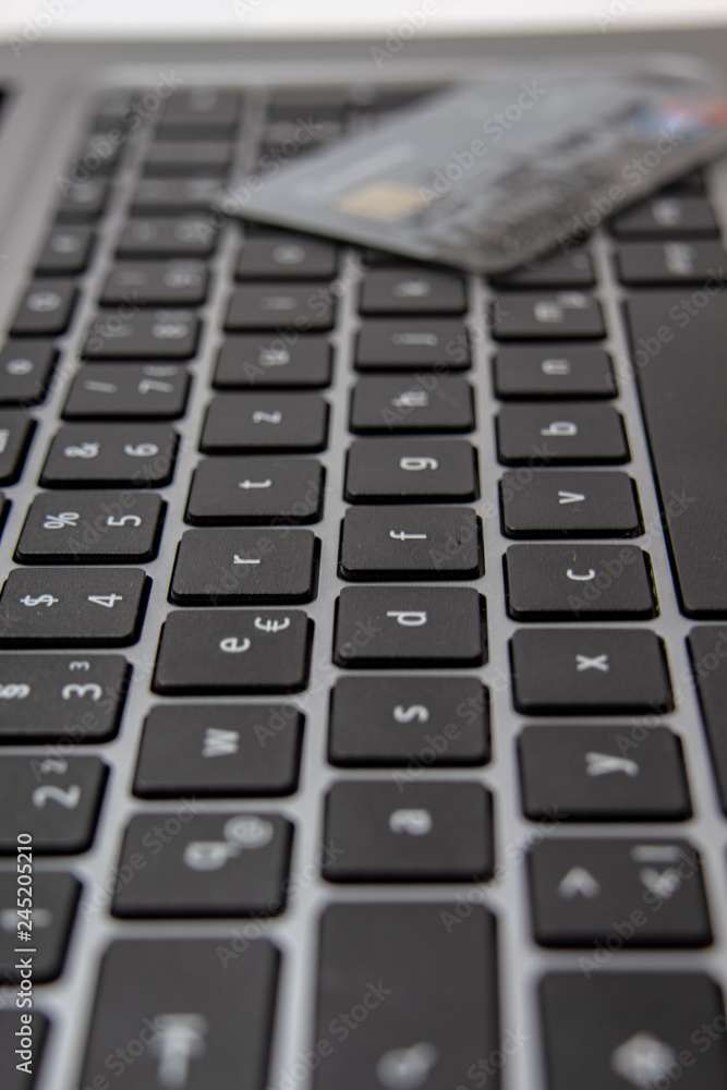 Ansicht einer schwarzen  Tastatur eines grauen Notebook mit Kreditkarte im Hintergrund