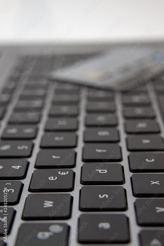 Ansicht einer schwarzen  Tastatur eines grauen Notebook mit Kreditkarte im Hintergrund