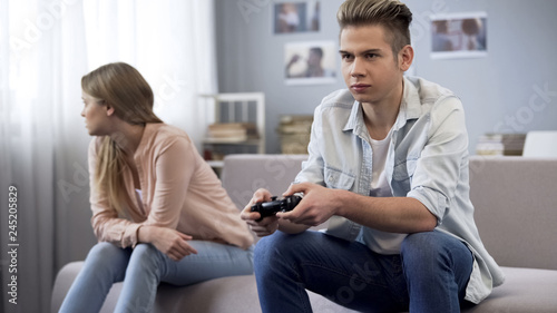 Offended girl turned away from boyfriend who indifferently playing video games