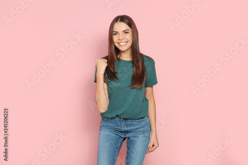 Young woman celebrating victory on color background