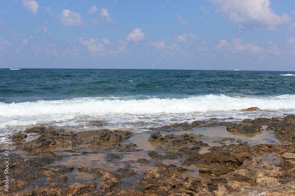 Rocky beach at low tide. Turquoise beautiful water. Restless waves. Clear blue sky. Cyprus, Paphos, Mediterranean sea.