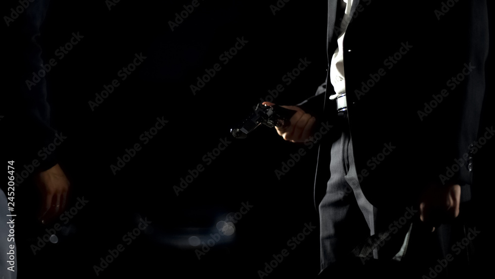 Illegal weapon trafficking, man in suit checking handgun holding bag with money