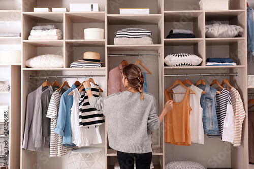 Photo Woman choosing outfit from large wardrobe closet with stylish clothes and home s