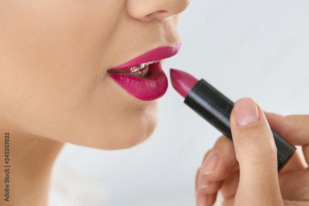 Beautiful woman applying lipstick on light background, closeup