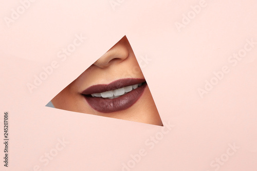Lips of beautiful young woman with dark lipstick visible through hole in color paper