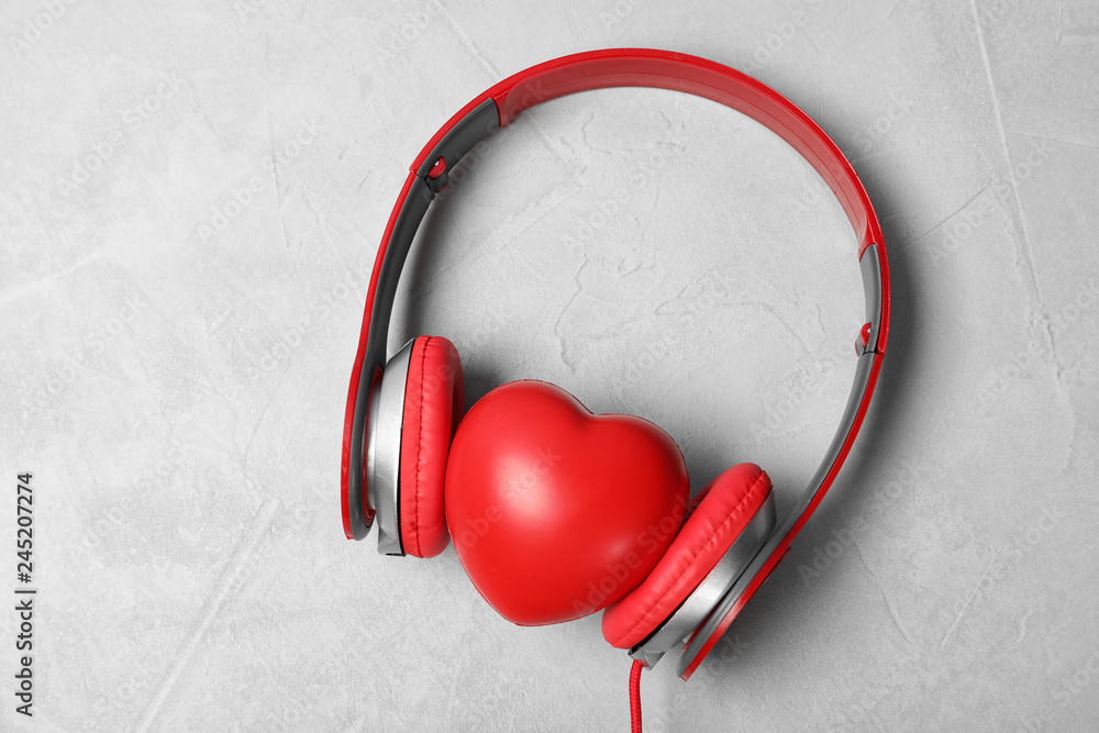 Headphones and heart on grey background, top view