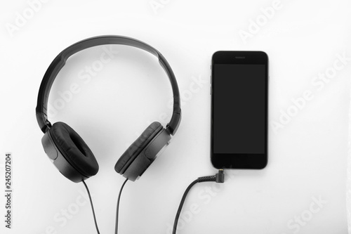 Smartphone with blank screen and headphones on white background, top view