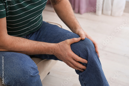 Senior man suffering from knee pain at home, closeup