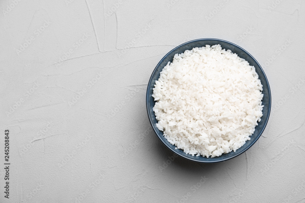 Bowl of boiled rice on color background, top view with space for text