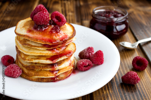 Homemade pancakes with raspberry jam in the white plate on the brown wooden background