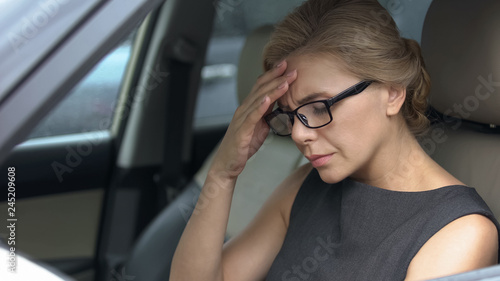 Blond woman in eyeglasses sitting on driver place and feeling terrible headache