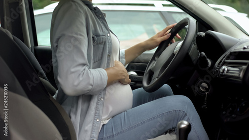 Pregnant woman in car, holding hand on belly, active baby during third trimester © motortion