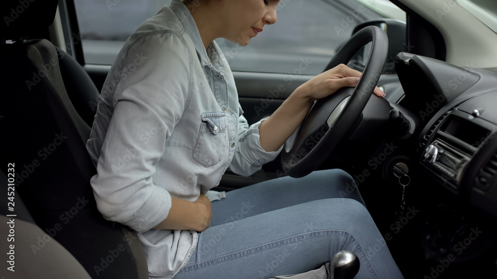 Woman in car feeling lower abdominal premenstrual pain, hormonal problems