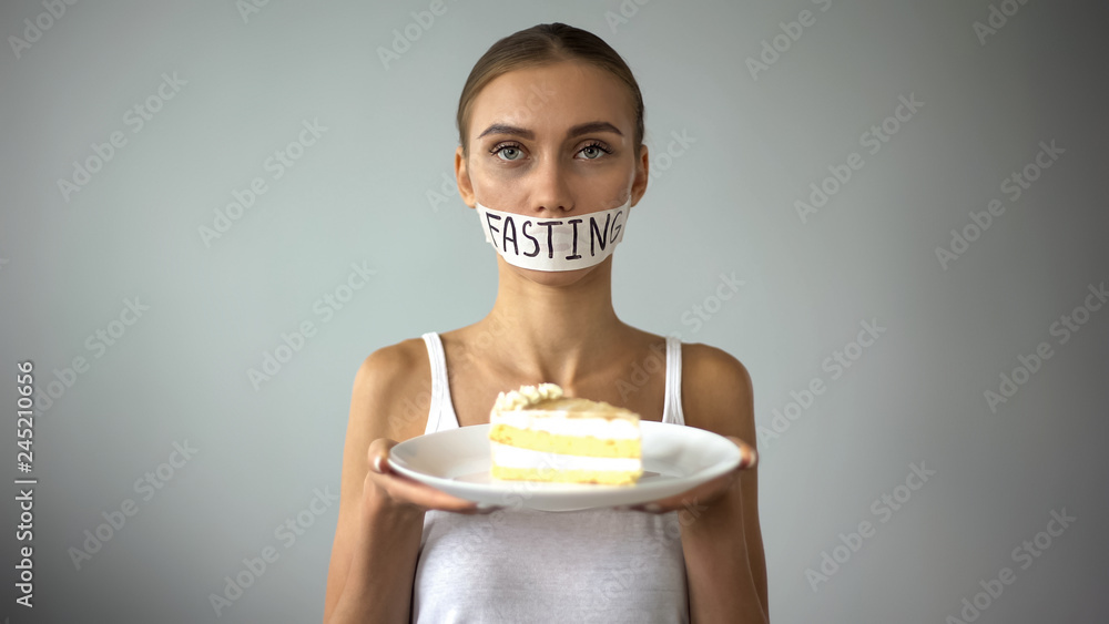 Anorexic girl holding pie, fasting word written on taped mouth, ban on sweets Anorexic girl holding pie, fasting word written on taped mouth, ban on sweets