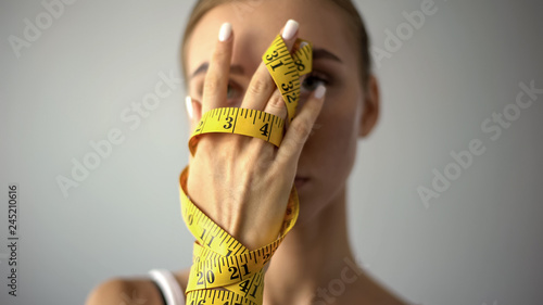 Anorexic model holding measuring tape, concept of harsh self-restriction in food photo