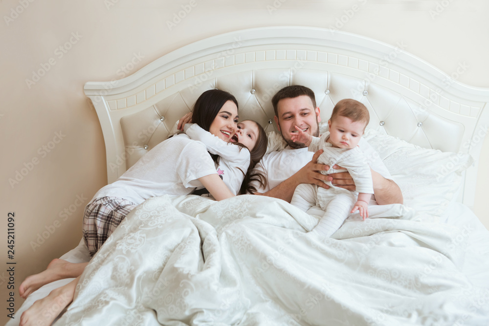  happy family is having fun together in bedroom. Family morning concept.   happy parents with two kids waking up in bed at home. 