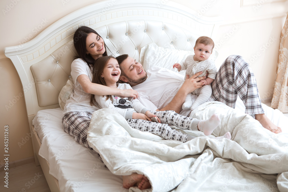  happy family is having fun together in bedroom. Family morning concept.   happy parents with two kids waking up in bed at home. 