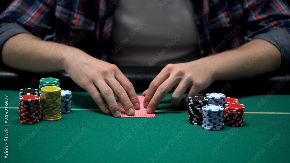 Young gambler ready to check his cards at casino poker game table, chance to win Young gambler ready to check his cards at casino poker game table, chance to win