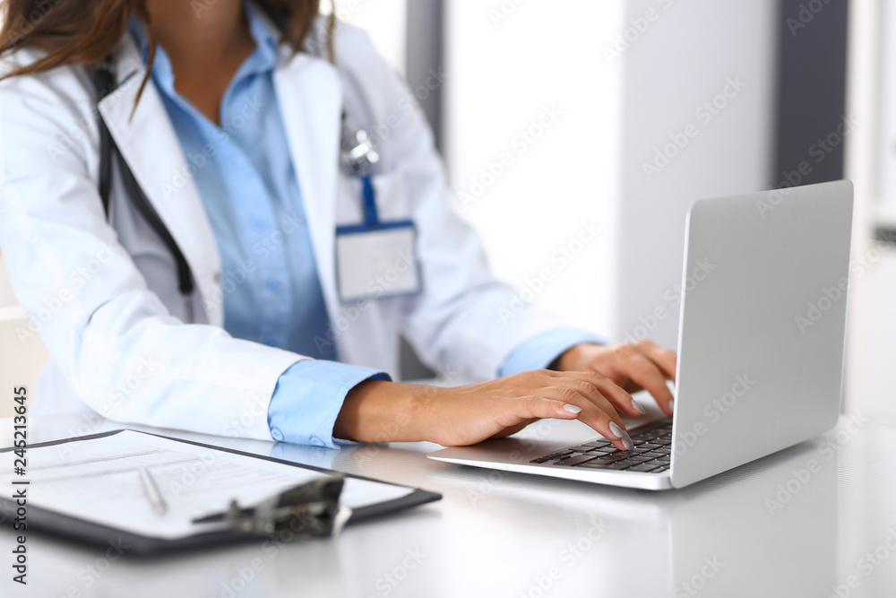 Unknown doctor woman typing on laptop computer while sitting at the desk in hospital office. close-up of hands. Physician at work. Medicine and health care concept Unknown doctor woman typing on laptop computer while sitting at the desk in hospital office. close-up of hands. Physician at work. Medicine and health care concept