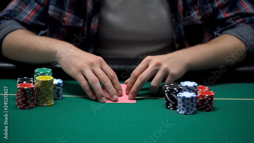 Young gambler ready to check his cards at casino poker game table, chance to win