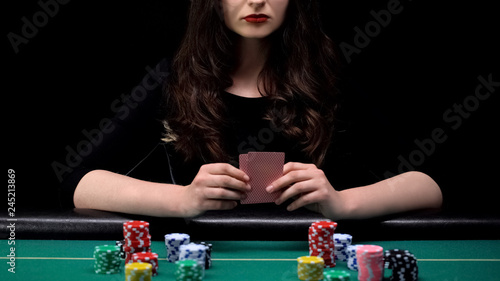 Fotografie Woman player checking her cards combination, bluffing at casino poker game