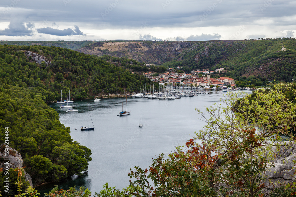 mountain valley with a very wide river, a village in the distance and a small harbor with many yachts and boats, the shores are overgrown with forests