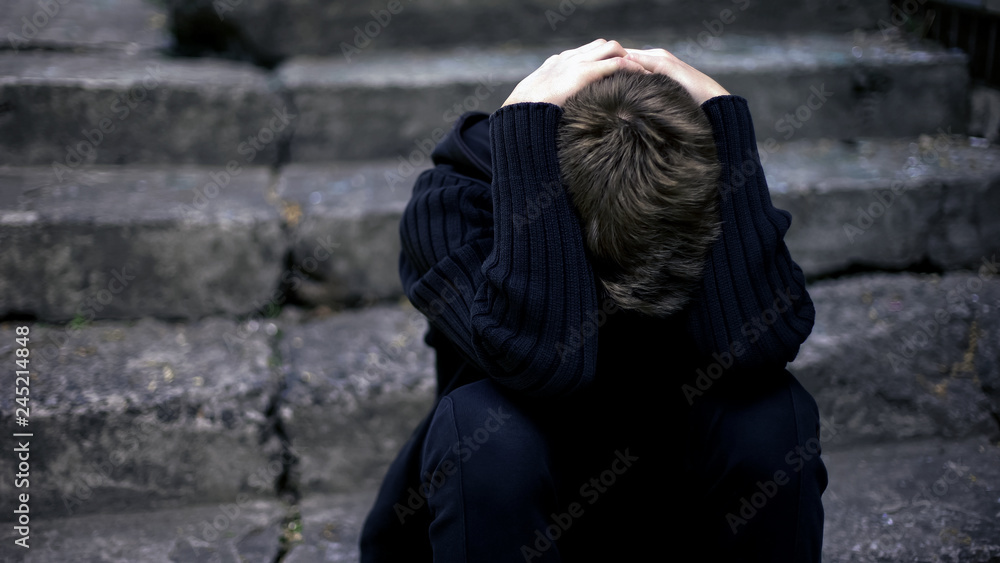 Lonely boy crying, sitting on old cracked steps, frightened war child, homeless