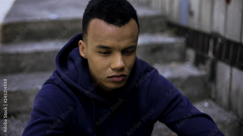 Hopeless afro-american teen sitting on steps in ghetto, concerned about future Hopeless afro-american teen sitting on steps in ghetto, concerned about future