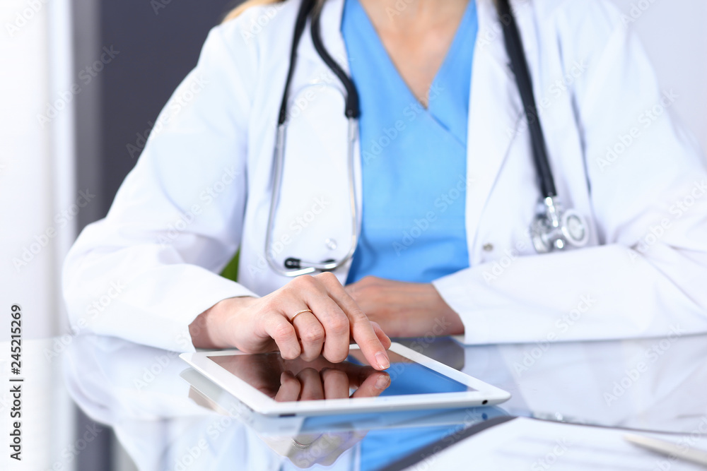 Woman doctor using tablet computer while sitting at the desk  in hospital office, closeup. Healthcare, insurance and medicine concept