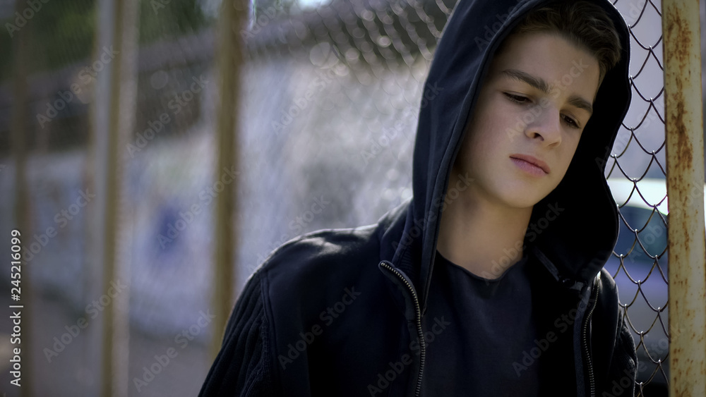Boy in hoodie leaning on fence, orphan in boarding school, confinement