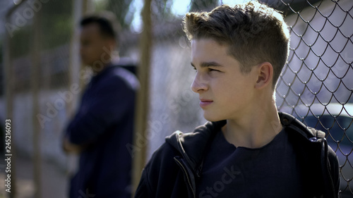 Thoughtful teen boys leaning on metal fence, upset with future, orphanage photo