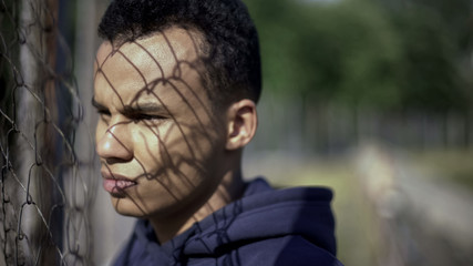 Afro-american boy watching rich district through fence, poverty, immigration