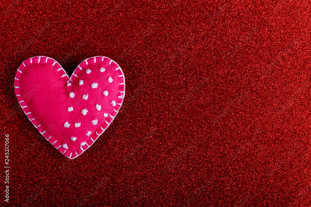 Obraz premium Red heart made of felt on a red background. Handmade blank for greeting card, copy space.