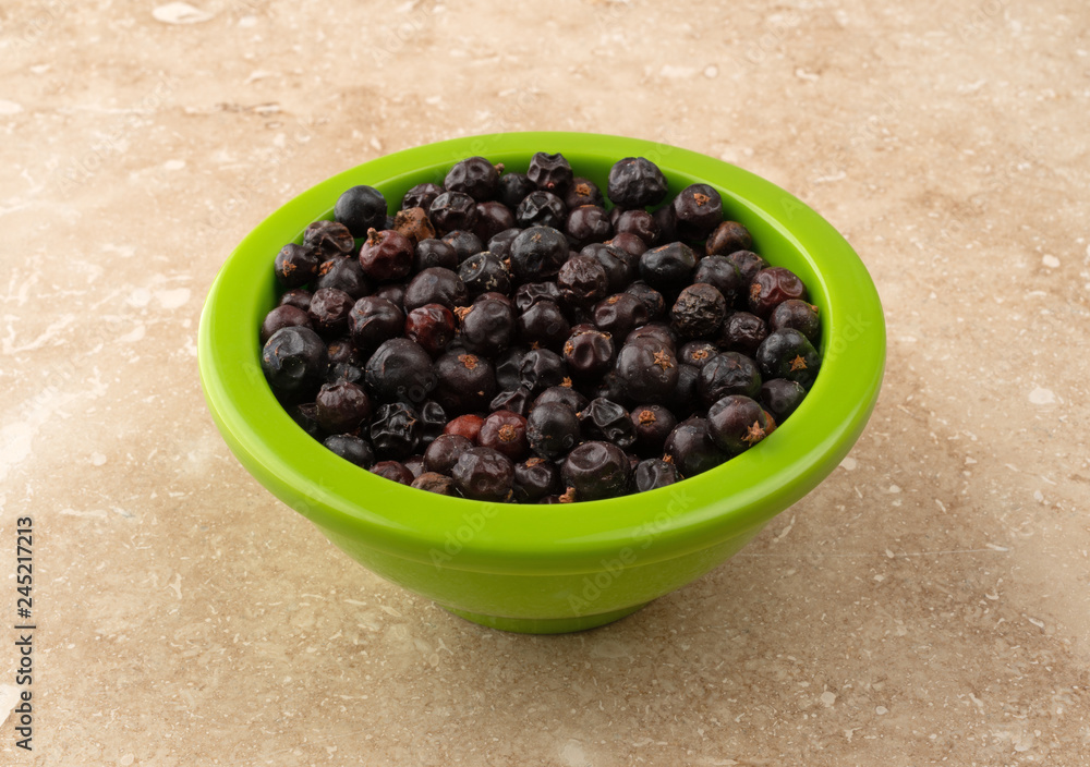 Bowl filled with juniper berries on a marble counter top Bowl filled with juniper berries on a marble counter top